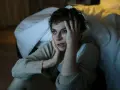 En kvinna sitter på golvet vid en säng, med händerna mot ansiktet, uttryckande episodisk paroxysmal ångest.