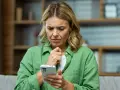 Kvinna med bekymrat ansikte tittar på sin mobiltelefon, en känsla av stark oro syns tydligt.