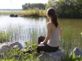 Kvinna sitter vid en sjö, omgiven av vass och stenar. En stund av avslappning mot ångest i naturens lugn.
