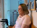 Äldre kvinna med glasögon sitter och funderar, kanske över ett hypokondri test. En rollator står bredvid.