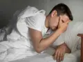 Man i sängen med handen mot pannan, upplever panikångest efter alkohol.