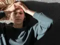 En ung person med hörlurar ligger på en grå yta, med händerna mot pannan. Kanske lyssnar hen på musik för att få bort ångest snabbt.