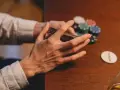 Händer som blandar kort vid ett pokerbord, med marker och en "dealer"-bricka. En påminnelse om att spelberoende behandling finns tillgänglig.
