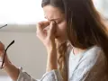 Kvinna med glasögon i handen, gnuggar sig i ögonen. Kanske tecken på muskelryckningar stress.