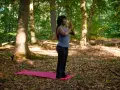 Kvinna i skogen på en yogamatta, med händerna i bön. En stund av avslappning och lugn för att minska stress.
