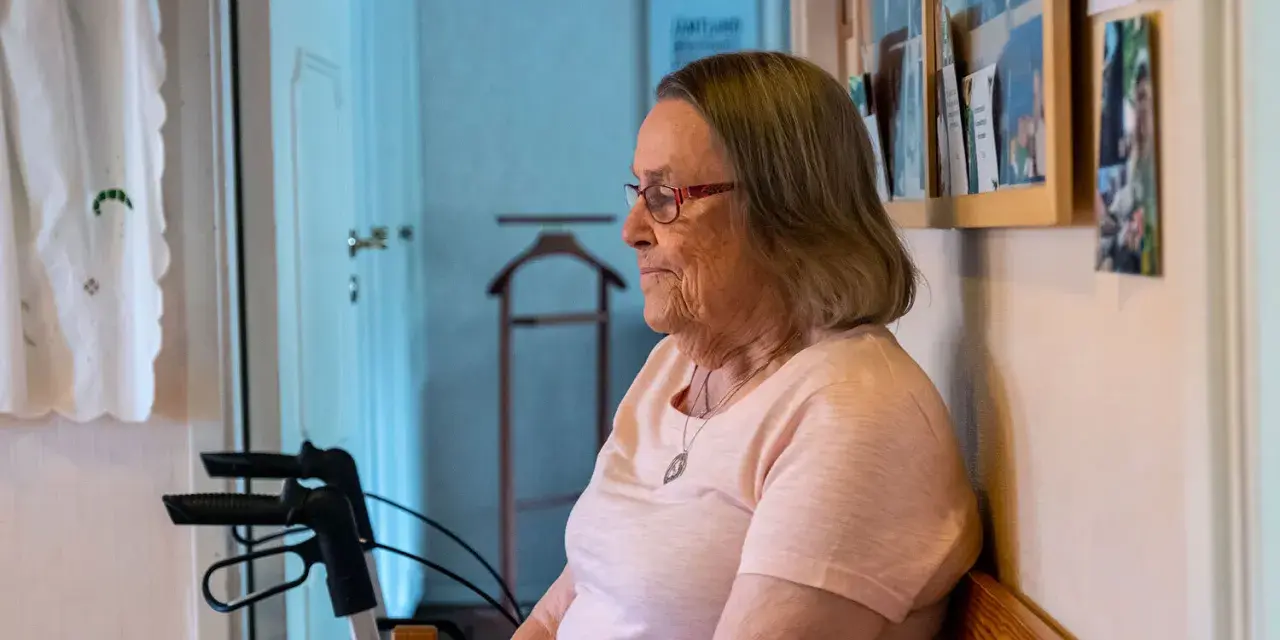 Äldre kvinna med glasögon sitter och funderar, kanske över ett hypokondri test. En rollator står bredvid.