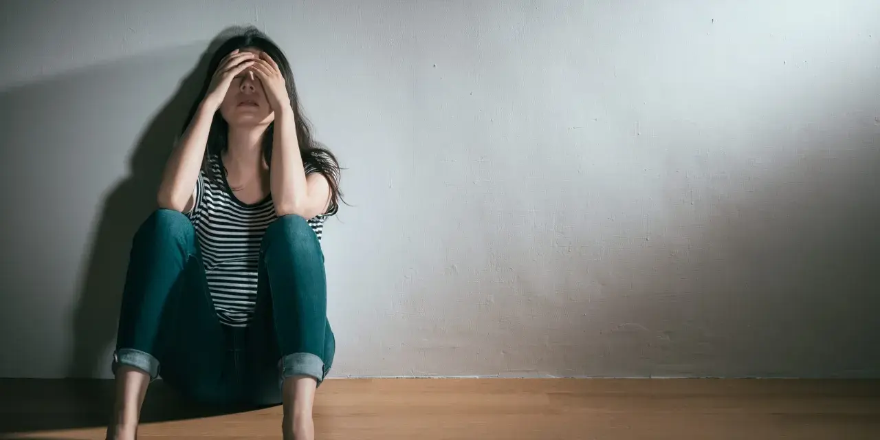En kvinna sitter på golvet med händerna över ansiktet, en bild som symboliserar grov depression och ensamhet.