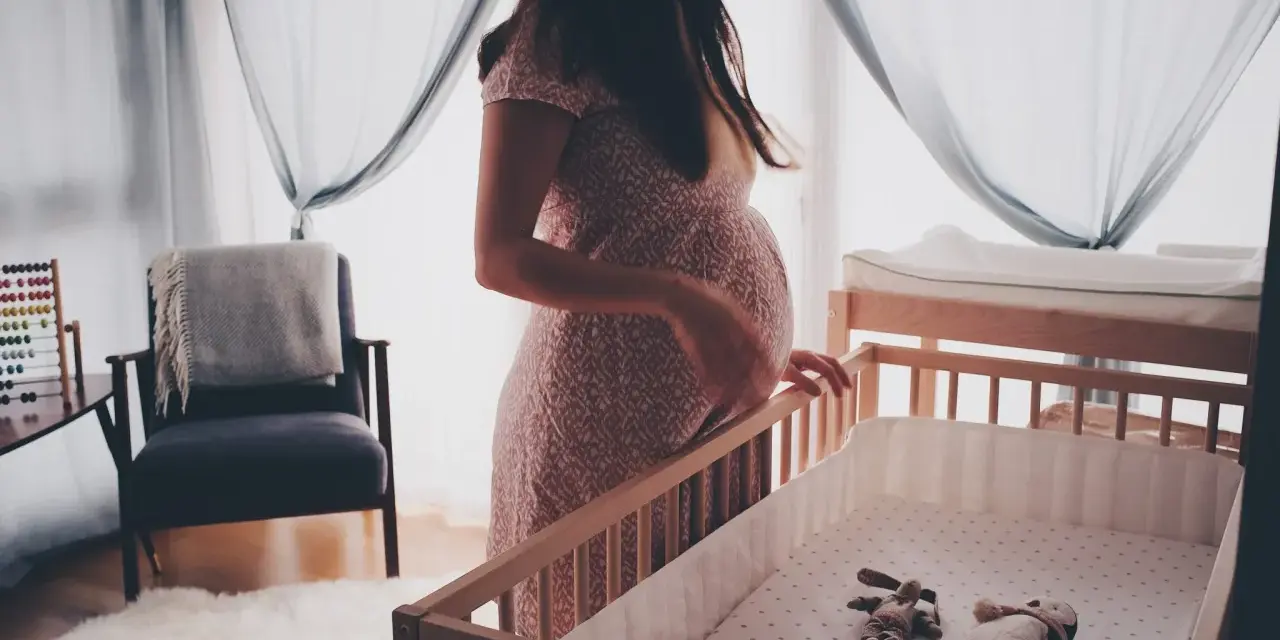 En gravid kvinna vid en spjälsäng, med en känsla av oro som kan associeras med gravid depression.