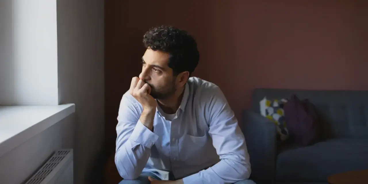 En man sitter ensam vid ett fönster, med handen mot hakan, blicken fjärran. Det är så pratar en deprimerad person, i tystnad och tankar.