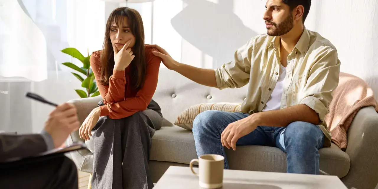 En man lägger en tröstande hand på en kvinnas axel under ett terapisamtal, vilket illustrerar en komplex medberoende relation.