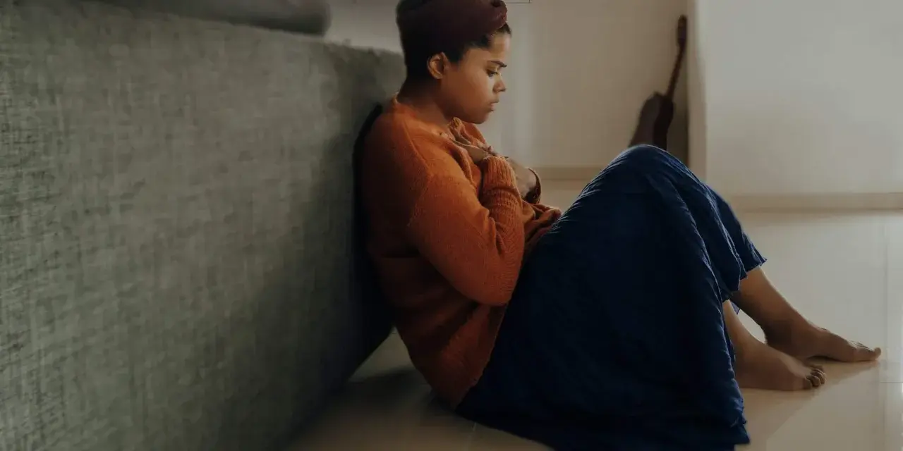 En kvinna sitter på golvet, med händerna över bröstet, som om hon upplever ett gad symptom.