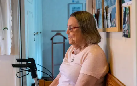 Äldre kvinna med glasögon sitter och funderar, kanske över ett hypokondri test. En rollator står bredvid.
