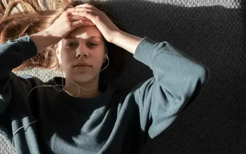 En ung person med hörlurar ligger på en grå yta, med händerna mot pannan. Kanske lyssnar hen på musik för att få bort ångest snabbt.