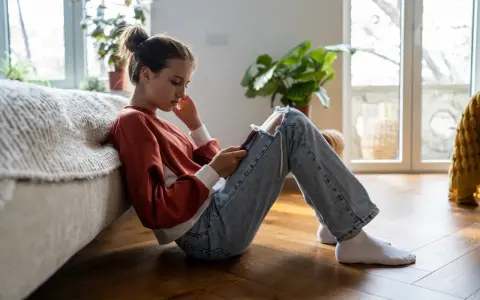 En ung tjej sitter på golvet, försjunken i sin telefon. Hennes hållning och ansiktsuttryck kan tyda på depression hos barn.