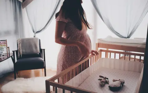 En gravid kvinna vid en spjälsäng, med en känsla av oro som kan associeras med gravid depression.