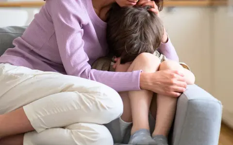 En mamma tröstar sitt ledsna barn på en soffa. Hon håller om honom med kärlek.