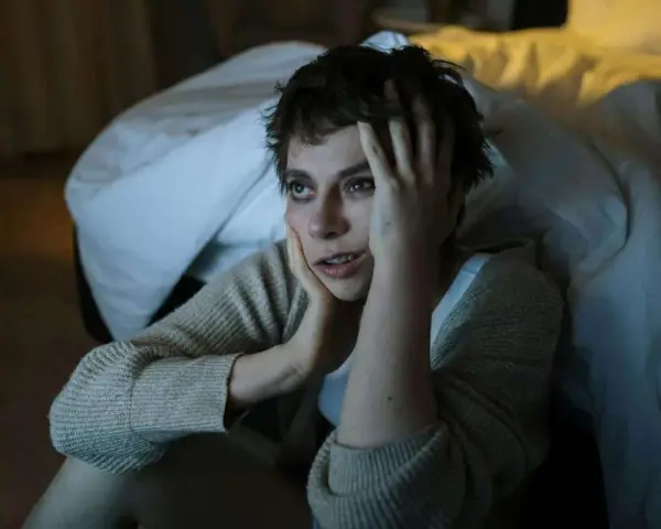 En kvinna sitter på golvet vid en säng, med händerna mot ansiktet, uttryckande episodisk paroxysmal ångest.