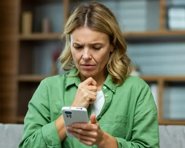 Kvinna med bekymrat ansikte tittar på sin mobiltelefon, en känsla av stark oro syns tydligt.
