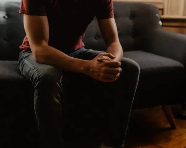 En person sitter på en soffa med händerna knäppta, kanske i väntan på ett generaliserat ångestsyndrom test.