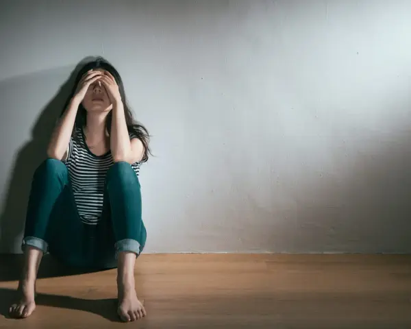 En kvinna sitter på golvet med händerna över ansiktet, en bild som symboliserar grov depression och ensamhet.