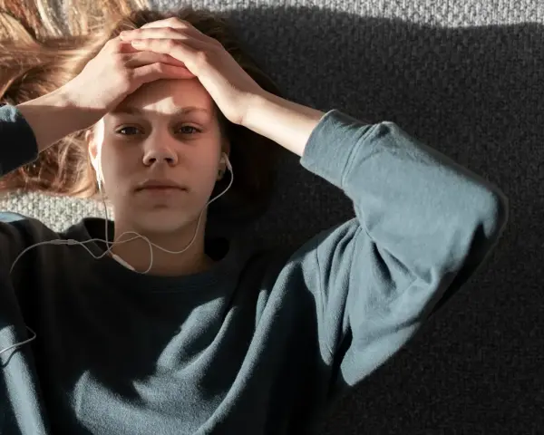 En ung person med hörlurar ligger på en grå yta, med händerna mot pannan. Kanske lyssnar hen på musik för att få bort ångest snabbt.