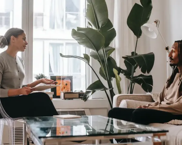 En kvinna och en man sitter mitt emot varandra i ett rum. Kvinnan håller en surfplatta och talar. Mannen lyssnar. Kanske diskuterar de hur mycket kostar terapi.