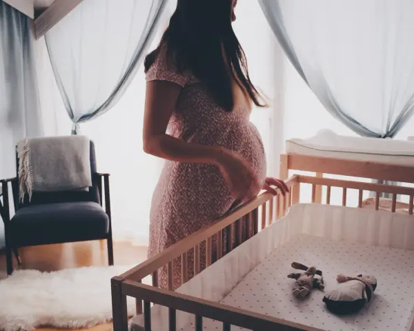 En gravid kvinna vid en spjälsäng, med en känsla av oro som kan associeras med gravid depression.