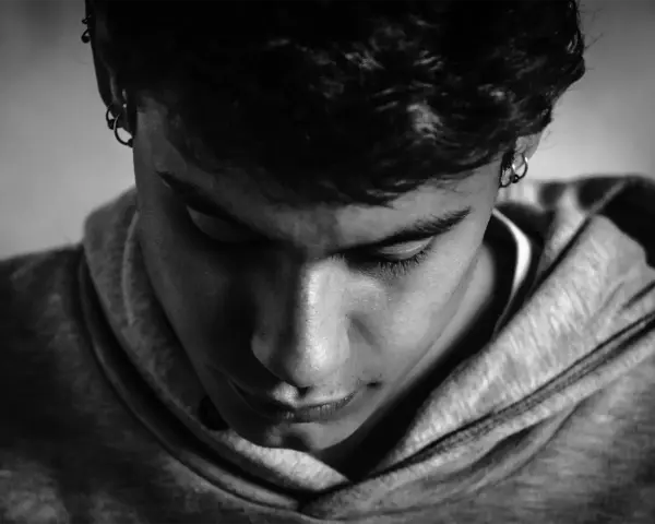 En ung person med örhängen i en hoodie, blicken nedåt. Kanske ett uttryck för dystymi symtom.