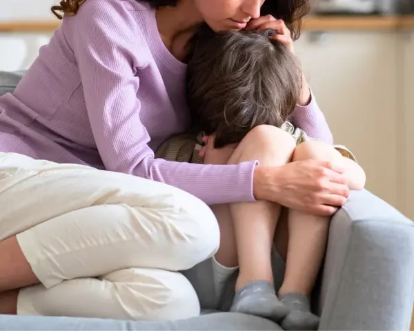 En mamma tröstar sitt ledsna barn på en soffa. Hon håller om honom med kärlek.