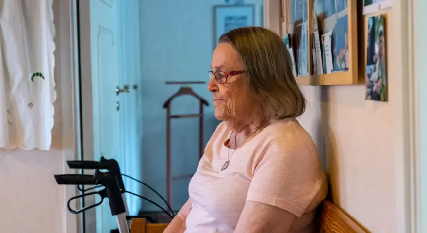 Äldre kvinna med glasögon sitter och funderar, kanske över ett hypokondri test. En rollator står bredvid.