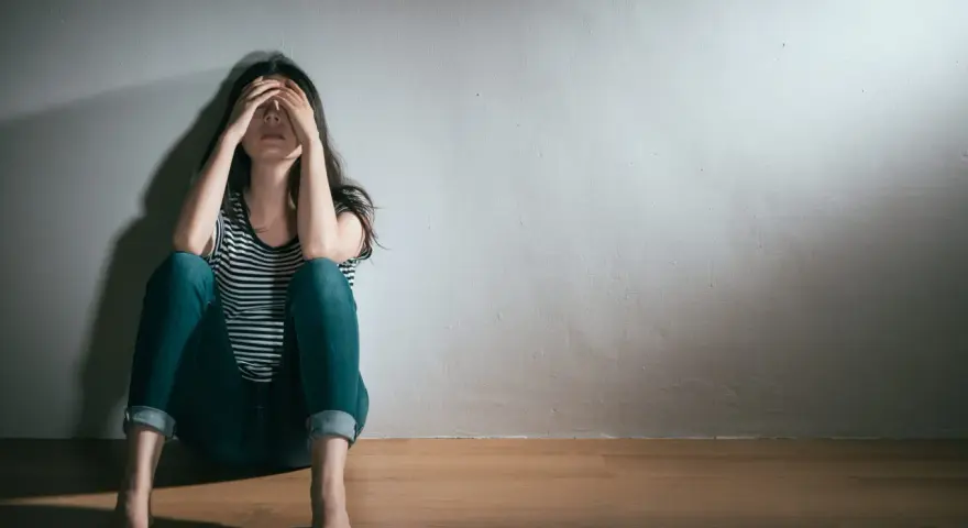En kvinna sitter på golvet med händerna över ansiktet, en bild som symboliserar grov depression och ensamhet.