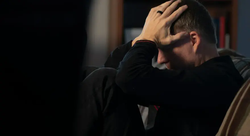 Man med händerna mot huvudet, djupt försjunken i tankar. En påminnelse om att bli mentalt stark genom svåra stunder.
