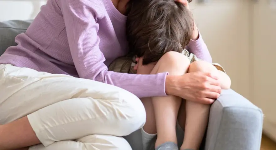 En mamma tröstar sitt ledsna barn på en soffa. Hon håller om honom med kärlek.