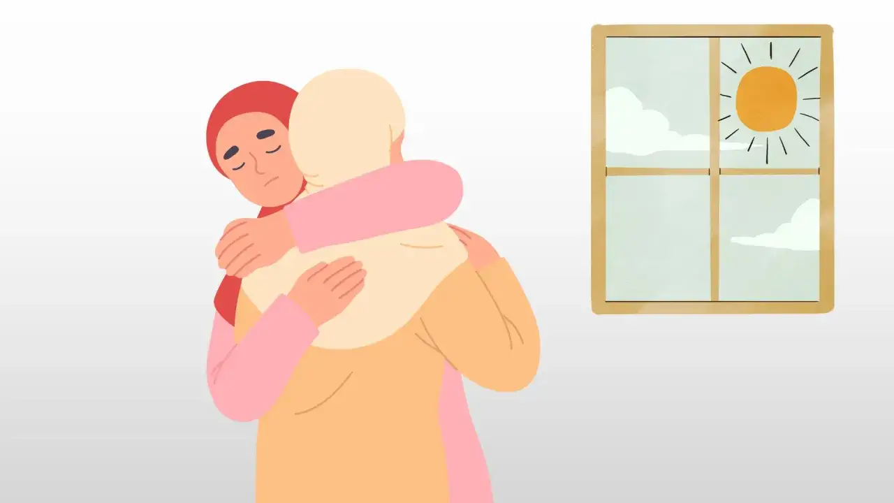 Två kvinnor kramas. En med röd hijab ser trött ut, den andra med ljus hijab tröstar. Solen skiner utanför fönstret, en påminnelse om att ta det less på livet.