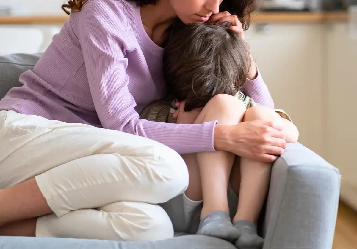 En mamma tröstar sitt barn som verkar ha en panikångestattack. Barnet kurar ihop sig i famnen medan mamman håller om det.