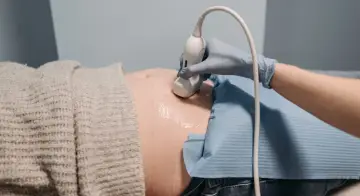 En hand i blå handske utför ultraljud på en gravid mage. En ny fas i livet, inte en gravid depression test.